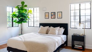 A bedroom with a bed, a nightstand, a lamp, a potted plant, and three framed pictures on the wall. - Private 2BR Duplex  Parking, W/D, Near Studios (Los Angeles)