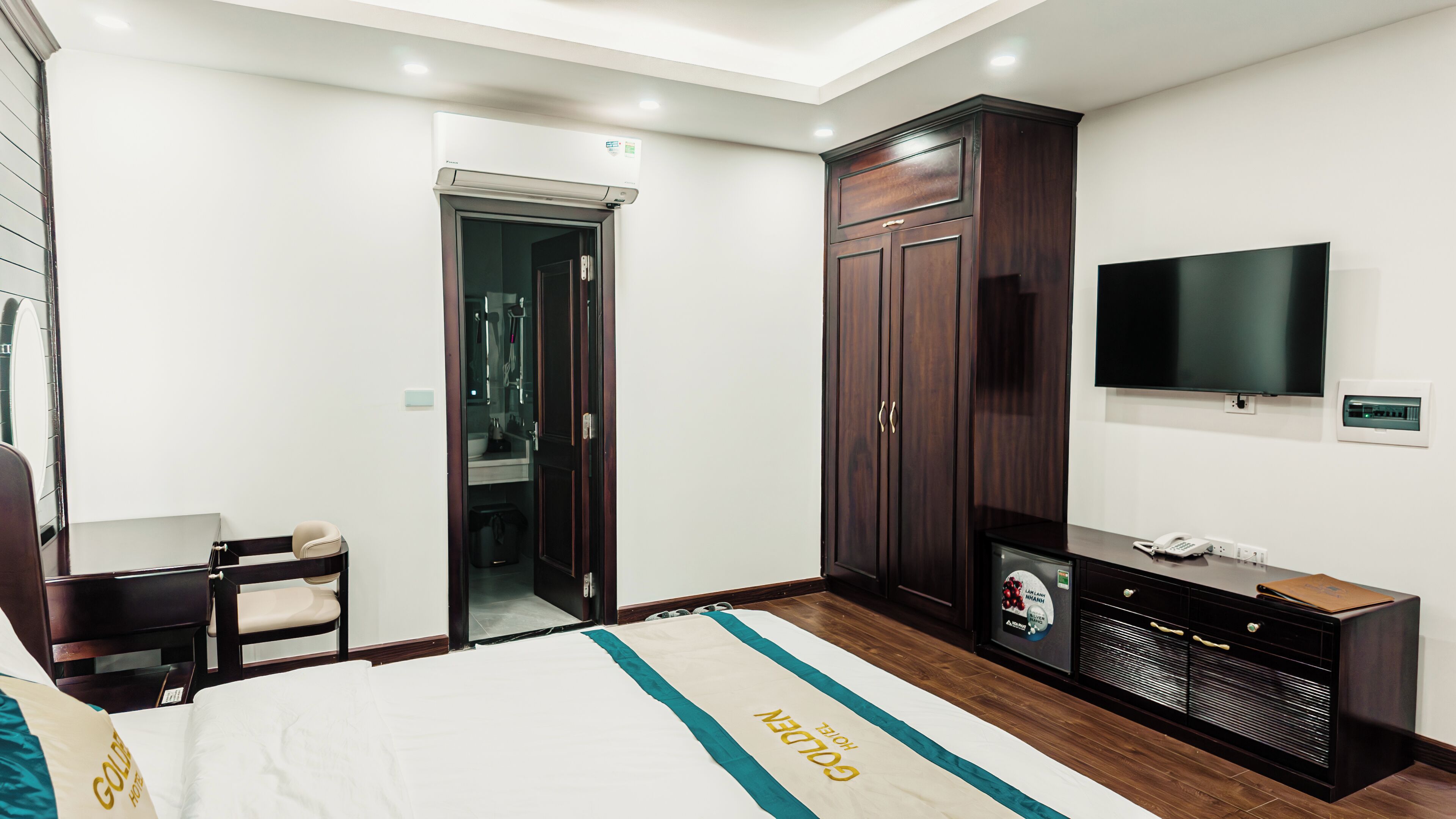 Habitación de hotel con cama, televisión, armario y baño visible a través de una puerta abierta.