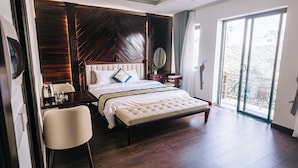 Habitación de hotel con una cama grande, un escritorio con silla, una mesita con planta y un balcón con vistas.