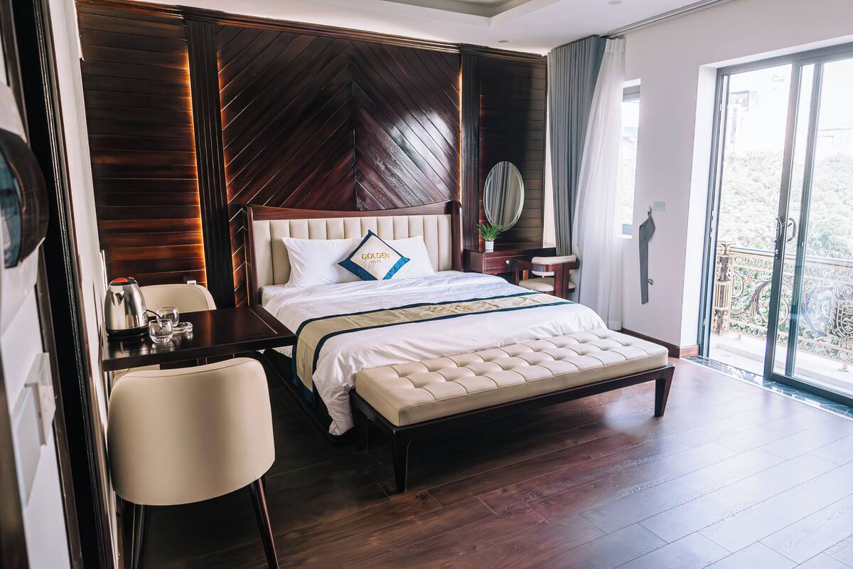 Ein Hotelzimmer mit einem großen Bett, einem Schreibtisch mit Stuhl, einem kleinen Tisch mit Pflanze und einem Balkon mit Blick.