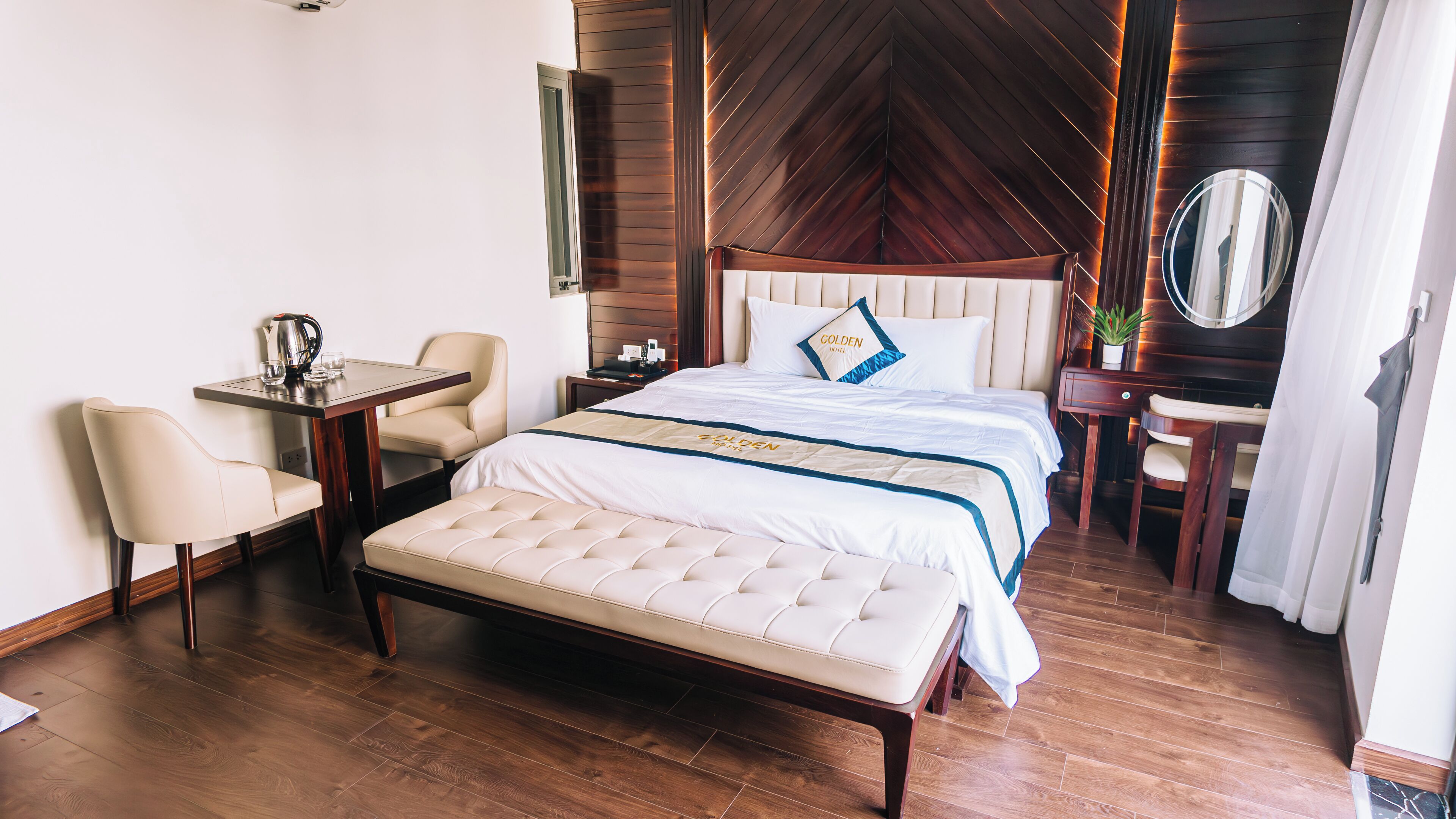 A hotel room with a large bed, a bedside table, a chair, a small desk, and a mirror.