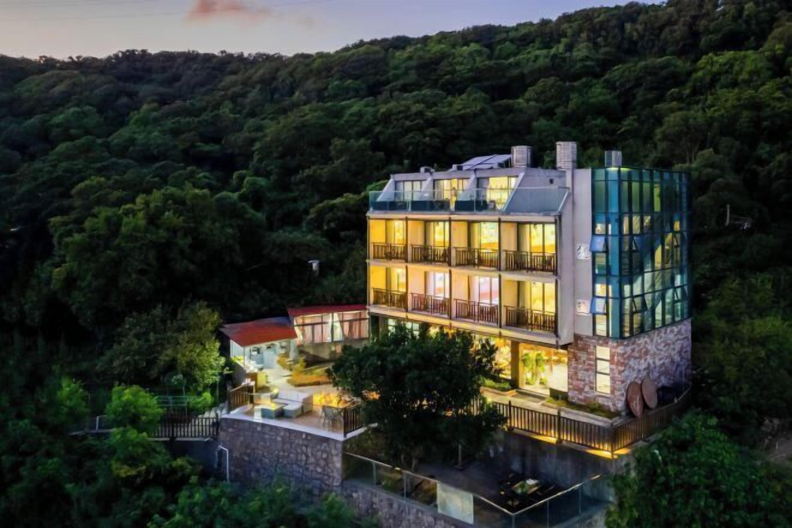 Un immeuble moderne à plusieurs étages, doté de balcons, entouré d’une forêt dense.