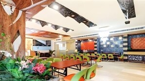 Un restaurante con techo de madera, sillas verdes y una maceta de piedra con plantas tropicales.