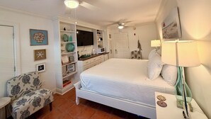 Un dormitorio con cama, una silla, un escritorio, un televisor y un ventilador de techo.