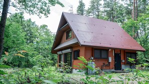 A single-story house with a sloped roof, surrounded by dense forest.