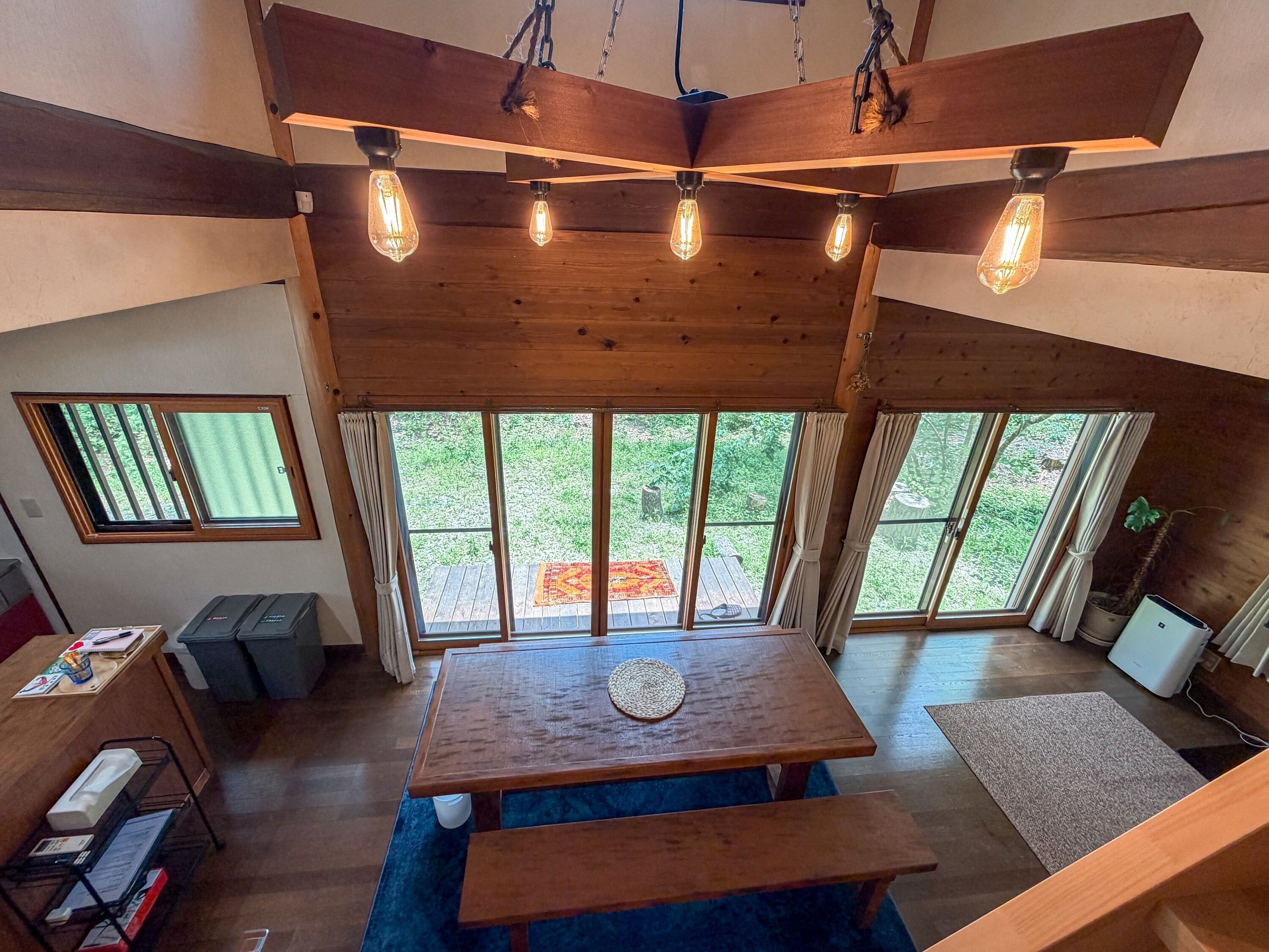 A wooden interior with a dining table, benches, and large windows.