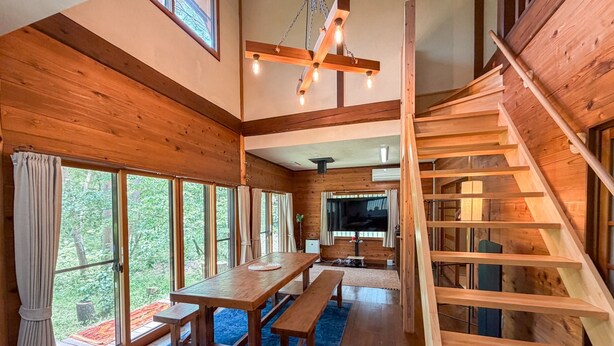 A wooden interior with a dining area, large windows, a staircase, and a TV.