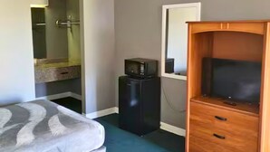 A hotel room with a bed, a wooden dresser, a television, and a bathroom with a shower. - Room 124 - 2 Double Beds (Livingston)