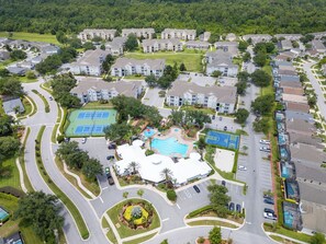 Vue aérienne d’un quartier résidentiel comprenant des immeubles d’appartements, une piscine, des courts de tennis et un parc aménagé.