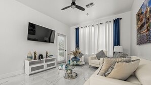 A modern living room with a white sofa, a glass coffee table, and a flat-screen TV mounted on the wall.