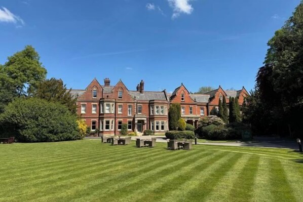 A large, red-brick building with a symmetrical facade, a well-maintained lawn, and a clear sky.