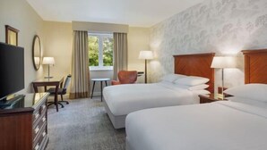 Une chambre d’hôtel avec deux lits, une télévision, un bureau, une chaise et une fenêtre avec des rideaux.