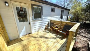 A wooden deck with a bench and a table, a white door with a wreath, and a small window. - Cozy & Stylish Home near Atlanta (Forest Park)