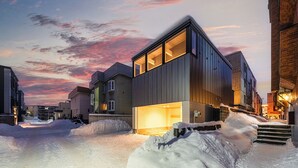 A modern building with large windows and a well-lit entrance, surrounded by snow-covered ground and other buildings. - THE REFLECT (Sapporo)