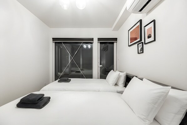 A modern hotel room with a large bed, a glass door leading to a bathroom, and a wall with framed artwork. - THE REFLECT (Sapporo)
