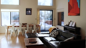 Ein geräumiger Wohnbereich mit großem Fenster, einem Esstisch mit Stühlen, einem schwarzen Ledersofa und einem Bild an der Wand.
