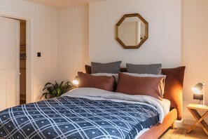 Ein Schlafzimmer mit einem Bett, einem Nachttisch mit Lampe, einem Spiegel an der Wand und einer Tür zu einem Kleiderschrank.