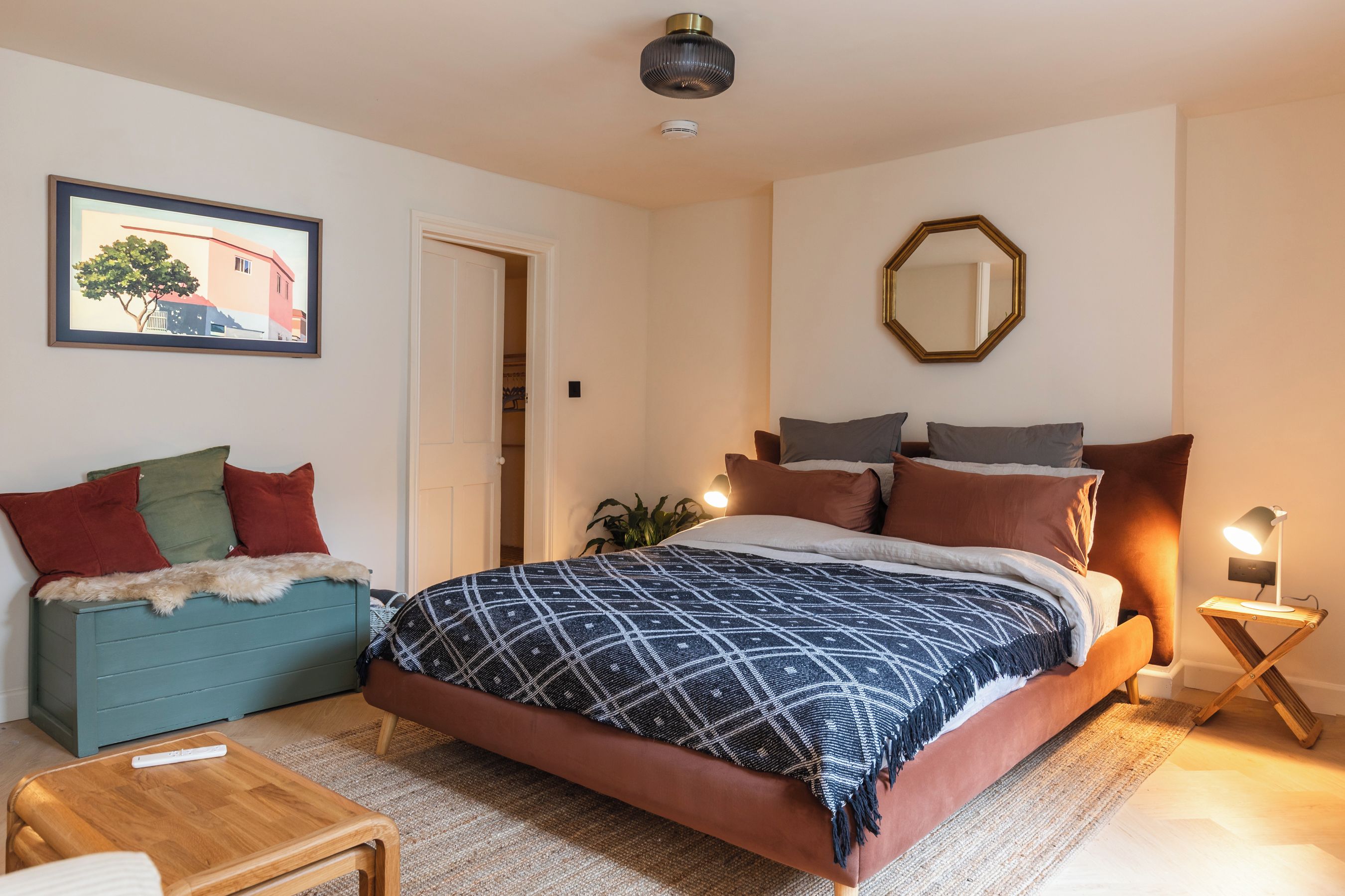 Ein Schlafzimmer mit einem Bett, einem Nachttisch, einem Sessel, einem kleinen Tisch, einem Spiegel und einem Bild an der Wand.