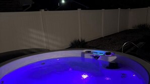 Een hottub met blauwe verlichting, omgeven door een witte hek en een grindpad.