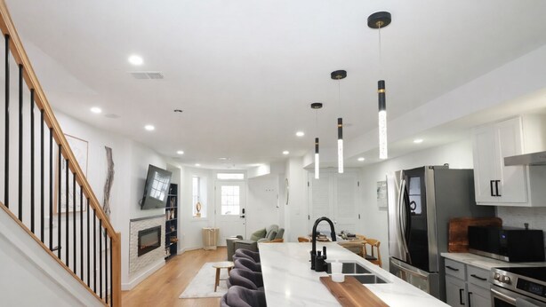Une cuisine moderne dotée d’un îlot central, d’appareils électroménagers en acier inoxydable et de luminaires suspendus.