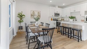 Een moderne keuken met witte kasten, een houten eettafel met stoelen, en een bar met barkrukken.