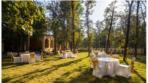 Een open evenementenruimte met ronde tafels en stoelen, omringd door bomen en een stenen gebouw.