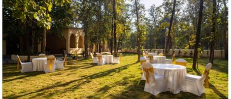 Un espace extérieur aménagé pour les événements, avec des tables et des chaises rondes, entouré d’arbres et d’une structure en pierre.