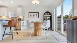 Een moderne keuken met een centraal eiland, witte stoelen en een houten tafel.
