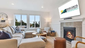 Een moderne woonkamer met een open haard, comfortabele zithoek en een televisie waarop 'Manzanita Beach Getaway Vacation Rentals' staat.