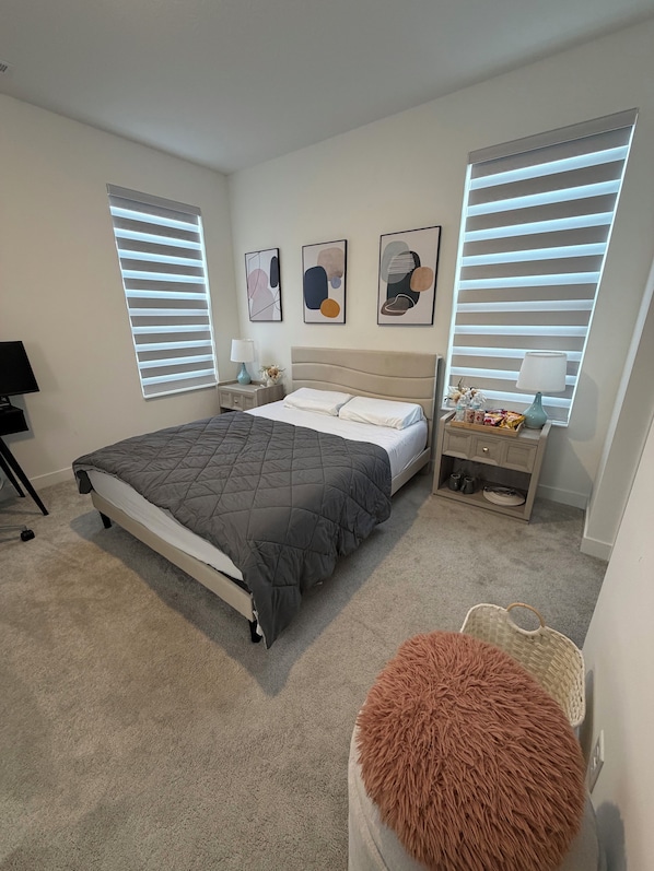 Un dormitorio con cama, mesitas de noche, una lámpara, un estante con objetos y una ventana con persianas.
