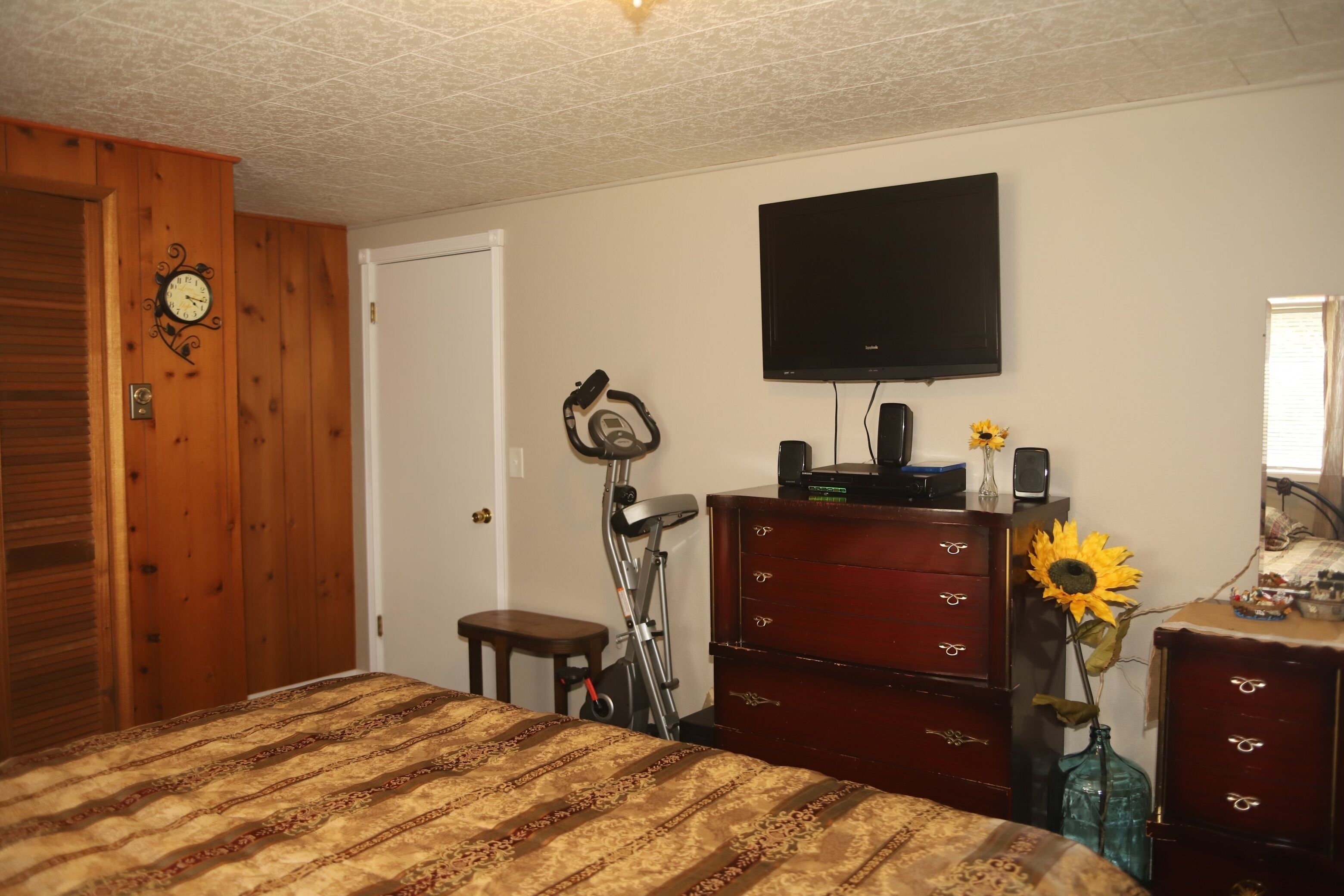 Un dormitorio con cama, cómoda, televisor y aspiradora.