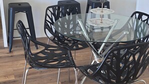 Eine moderne Küche mit weißen Schränken, einer Mikrowelle und einer Kaffeemaschine. Es gibt einen Essbereich mit einem Glastisch und schwarzen Stühlen.
