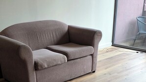 Ein Zimmer mit Holzboden und einem braunen Sofa an einer weißen Wand.