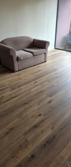 A room with a wooden floor and a brown sofa against a white wall. - Bright 2 b/room apartment -up to 6 guests-parking incl. Central to everything. (Melbourne)