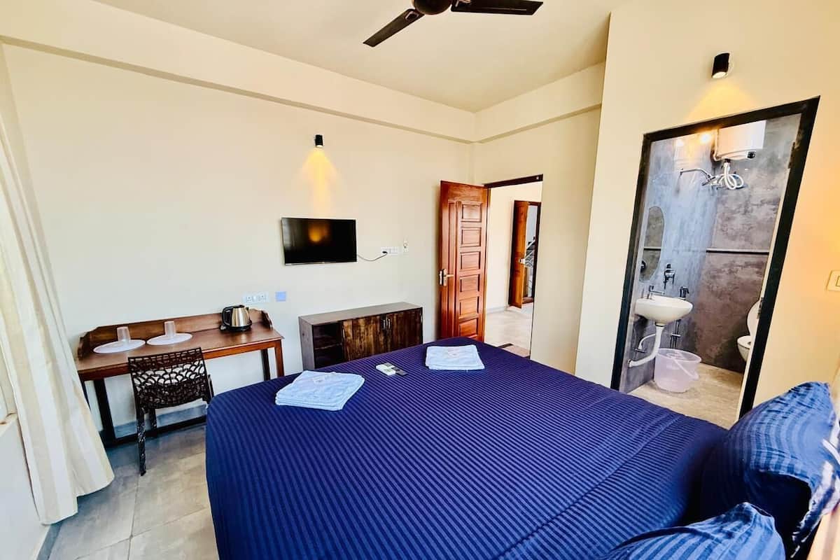 A hotel room with a bed, desk, chair, and a bathroom visible through an open door.
