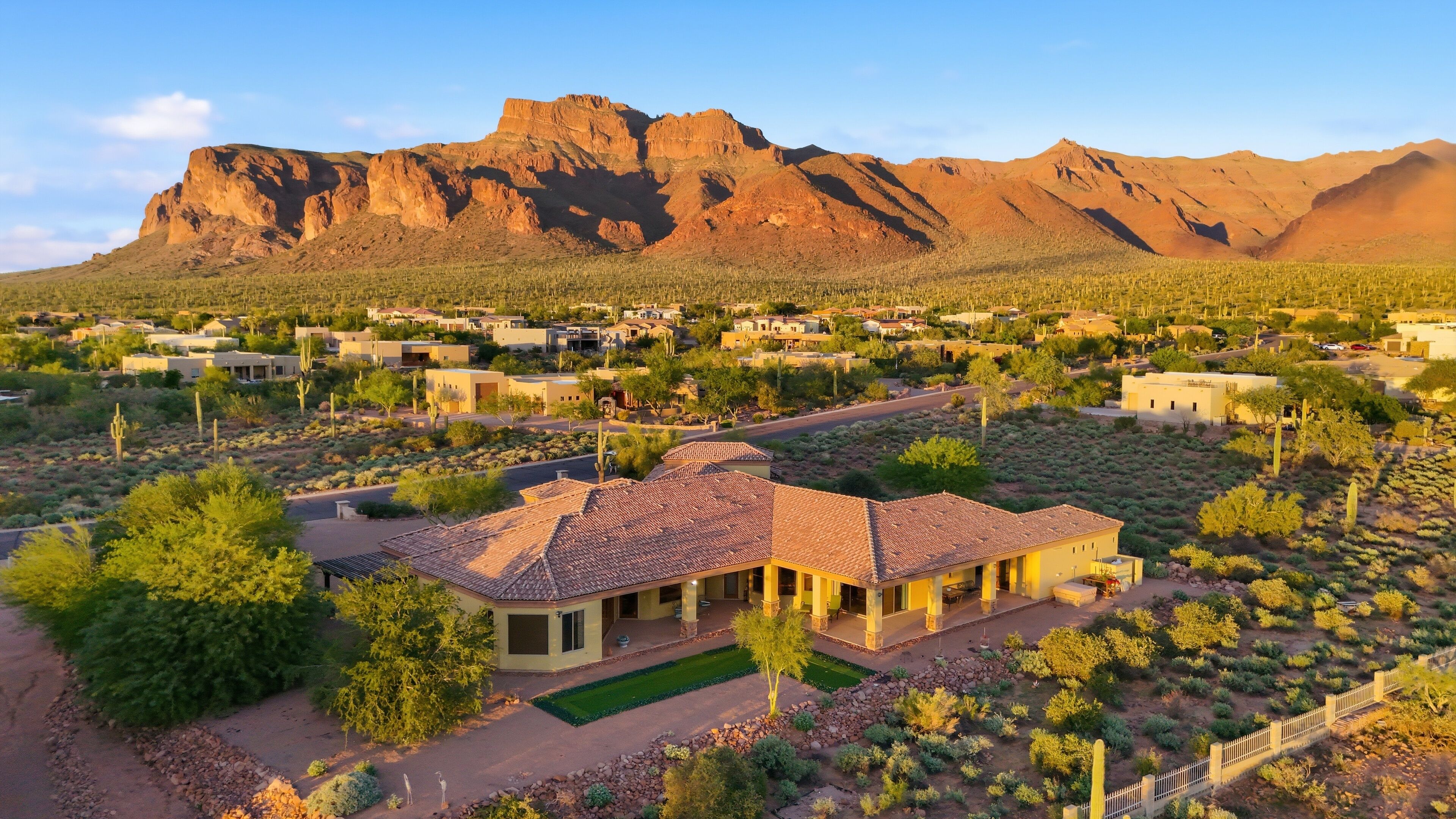 Zona residencial con una casa destacada de techo de tejas, rodeada de vegetación y cactus, con montañas al fondo.