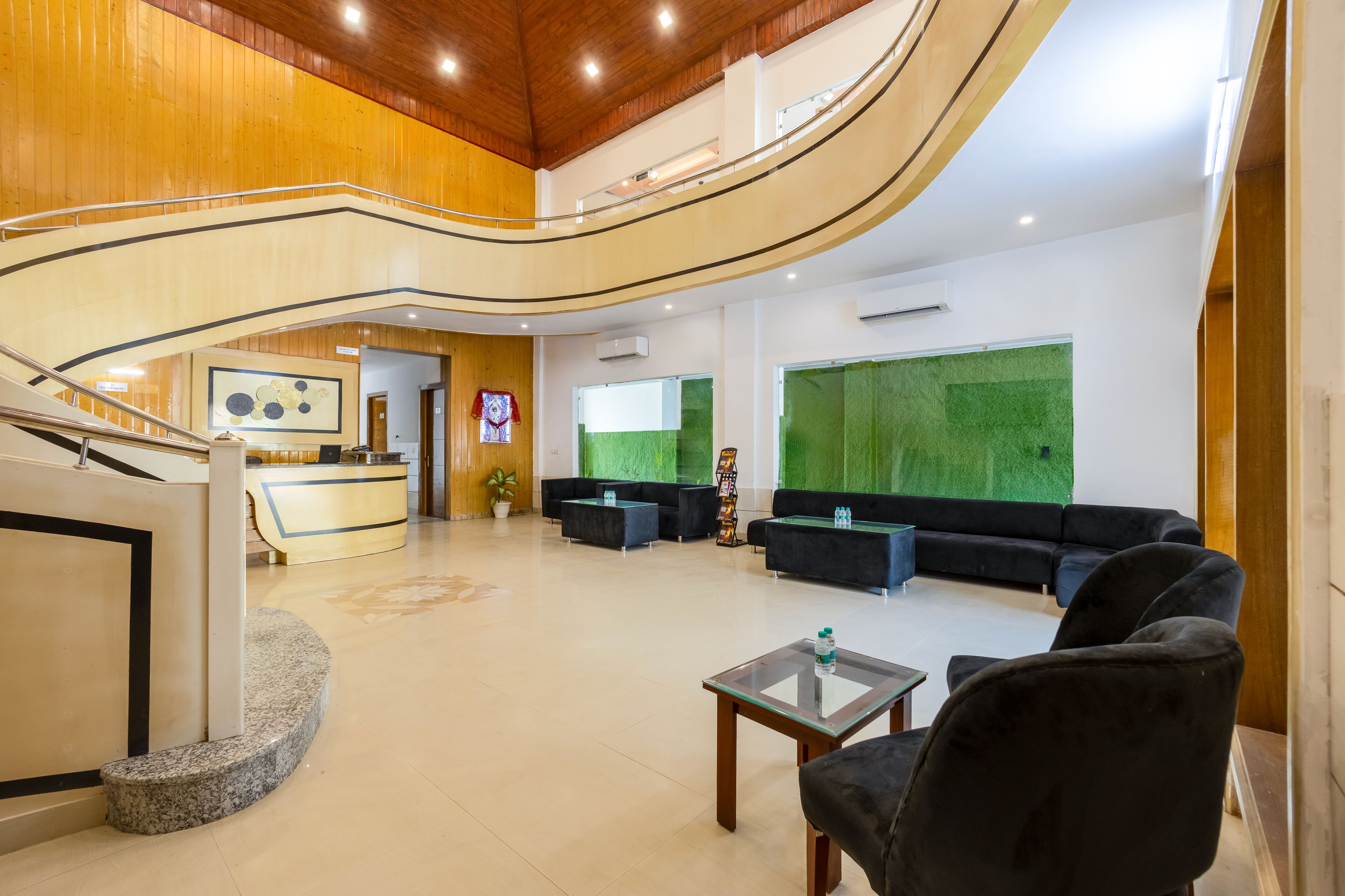 A spacious lobby with a reception desk, black sofas, a glass coffee table, and a green wall feature.