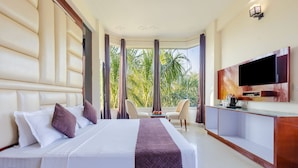Een hotelkamer met een groot bed, een televisie, een bureau en uitzicht op palmbomen.