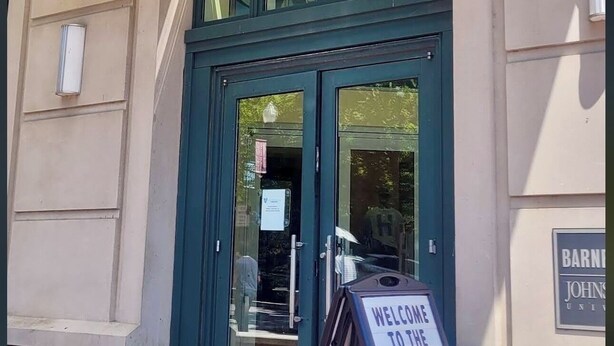 Ein Gebäudeeingang mit einem Schild, auf dem 'JOHNS HOPKINS' steht, und einem Willkommensschild für die neuen Gäste.