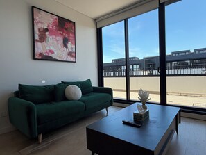 A modern living room with a green sofa, a coffee table with a remote control and a tissue box, and a large abstract painting on the wall.