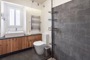 A modern bathroom with a wooden vanity, a white sink, a toilet, and a glass-enclosed shower area. - Casa Azul - Beach House (Ponta Delgada)