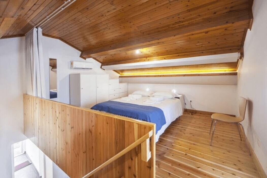 Ein Schlafzimmer mit Holzbalkendecke, einem Bett mit weißer Bettwäsche, einem Stuhl und Holzboden.
