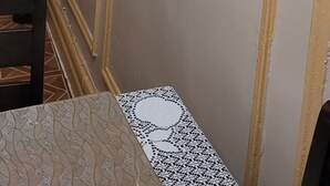 A room with a decorative wall, a table with a lace tablecloth, and a vase with dried plants.