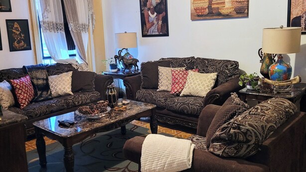A living room with two sofas, a coffee table, and a TV stand. There are decorative items on the coffee table, and a lamp on the TV stand.