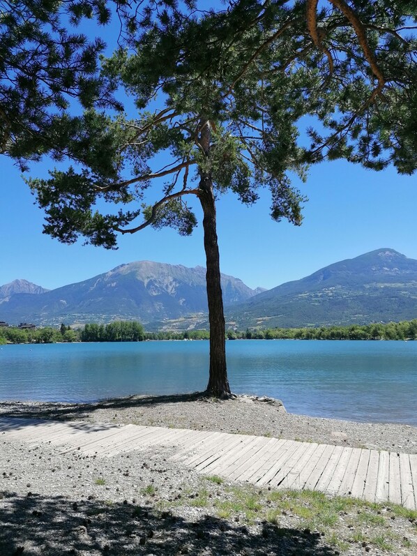 A lake with a wooden dock, a tree, and mountains in the background. - Spacious apartment Embrun (Embrun)