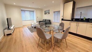 A modern living space with a dining area, a sofa, a TV, and a kitchen area with cabinets and a window.