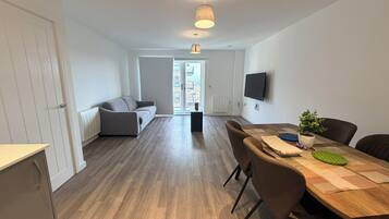 A modern apartment with a dining area, a sofa, a TV, and a view through a glass door.