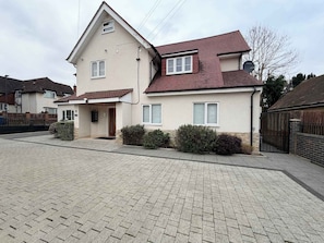 A two-story house with a brick roof, a small front porch, and a paved driveway. - Sleek Modern 2BDR Flat in Charming Pinner (Greater London)