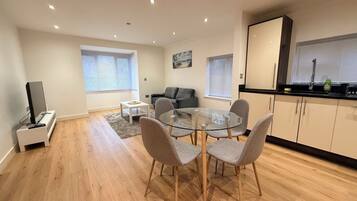 A modern living space with a dining area, a sofa, a TV, and a kitchen area with cabinets and a window.