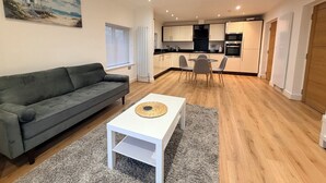 A modern living room with a grey sofa, a white coffee table, and a painting of a beach scene.